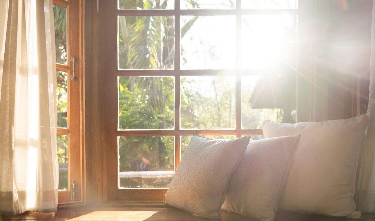 Three pillows on a seating bench beside a window.