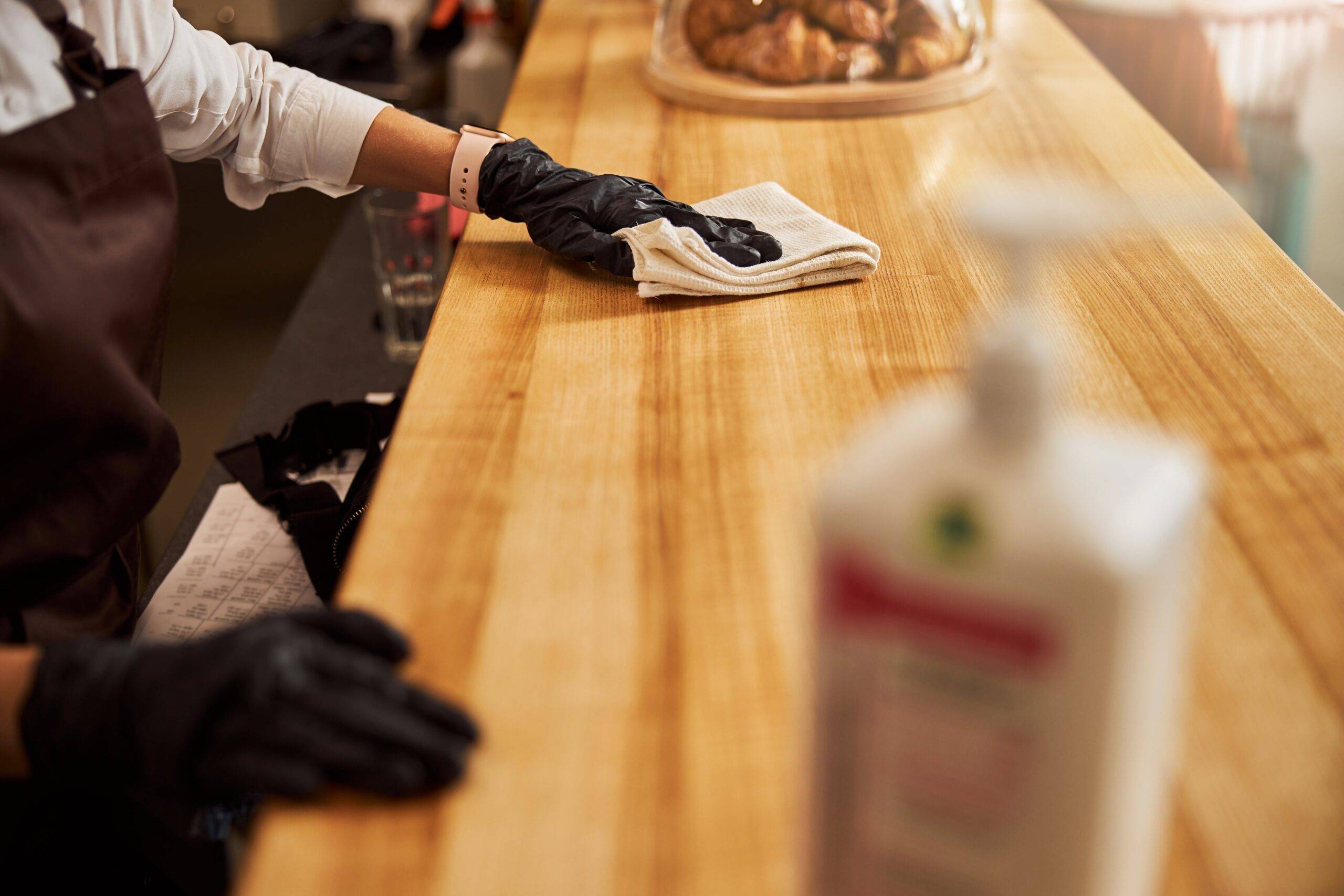 A person in black gloves wiping down a wood countertop.
