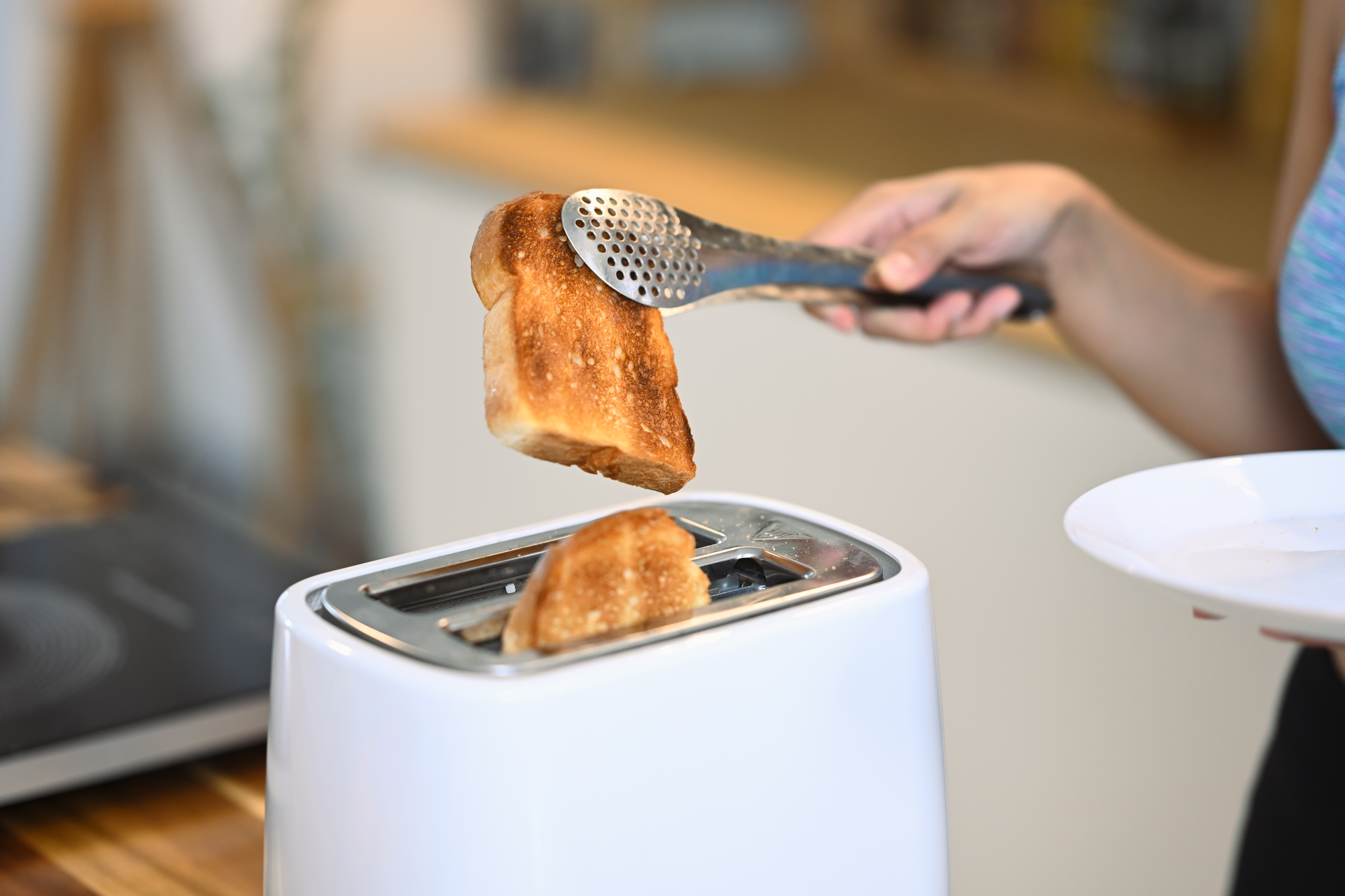 Shot pretty young woman in sports clothing toasting bread with toaster in the kitchen.