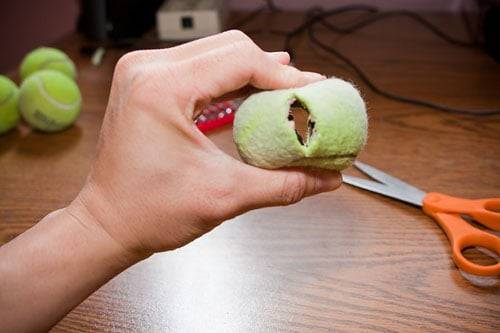 A hand squeezing a tennis ball after cutting a small opening into it.