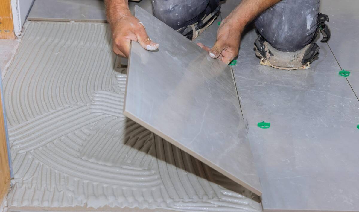 A pair of hands installing large floor tiles.