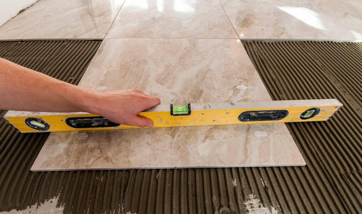A person holding a level on a large floor tile.