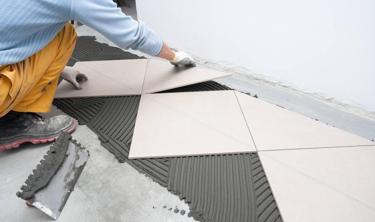 A person laying tile that's been cut to fit along the wall.