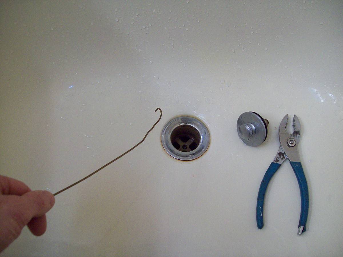 A person holding a bent wire hanger near a tub drain.