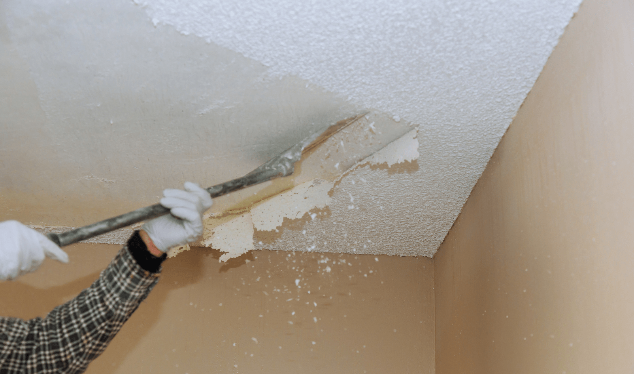 A person scraping a popcorn ceiling off with a scraper.
