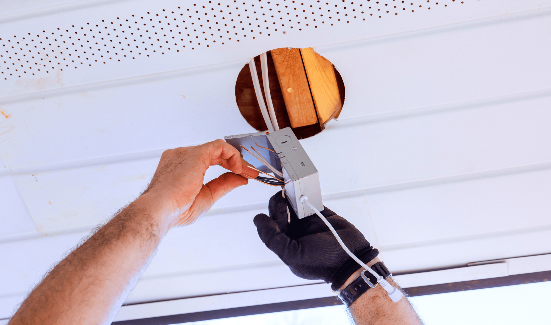 A pair of hands handling a wire box for a ceiling light fixture.