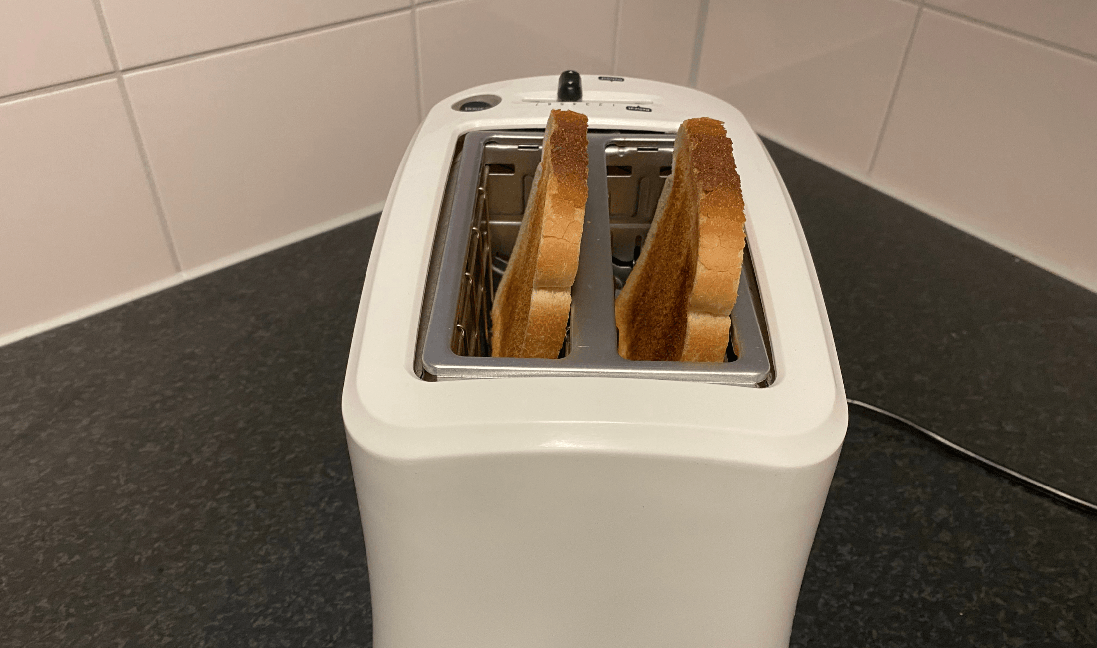 A toaster on a counter, showing two popped pieces of toasted bread.