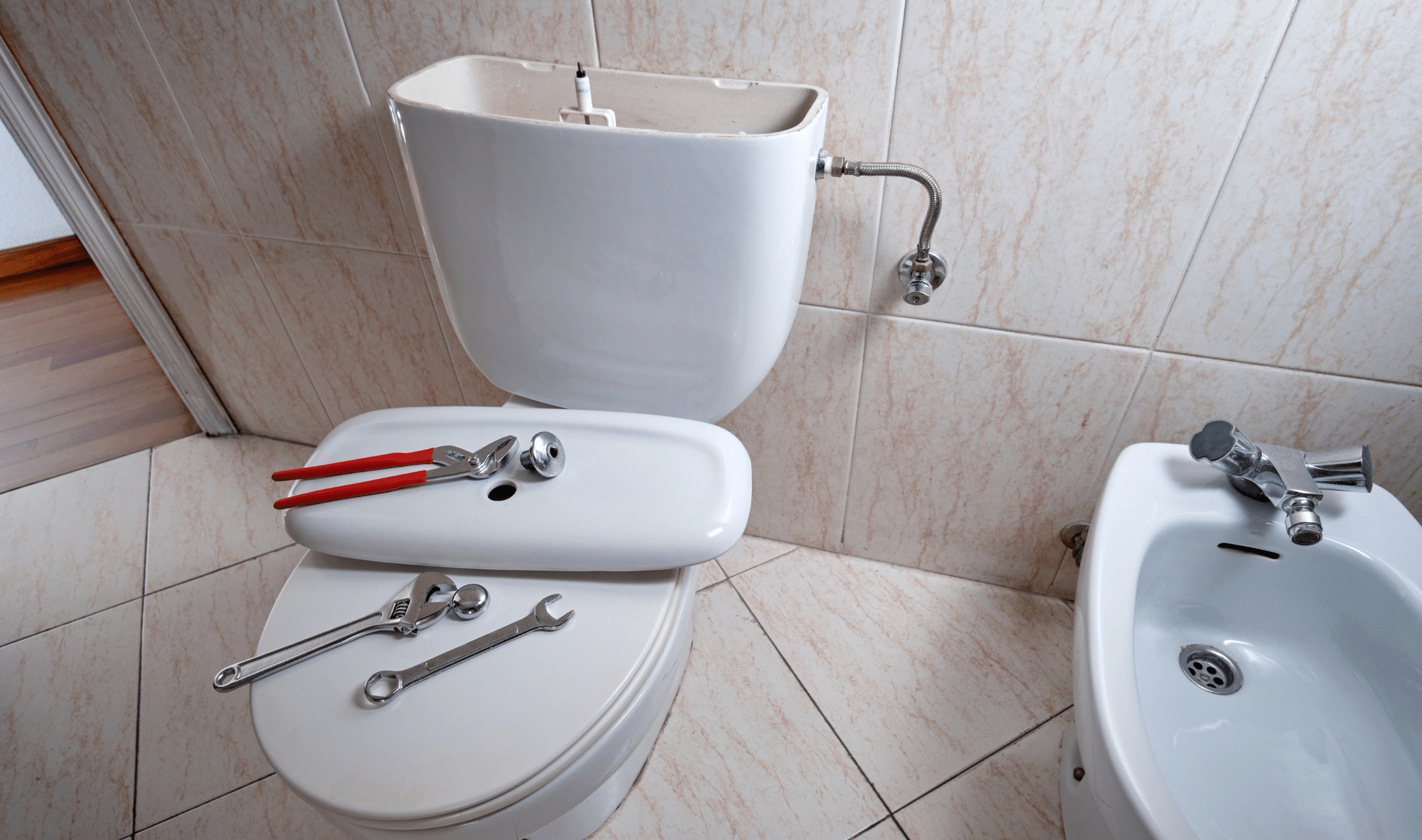 A toilet in a bathroom, the tank lid off, tools resting on the toilet lid.