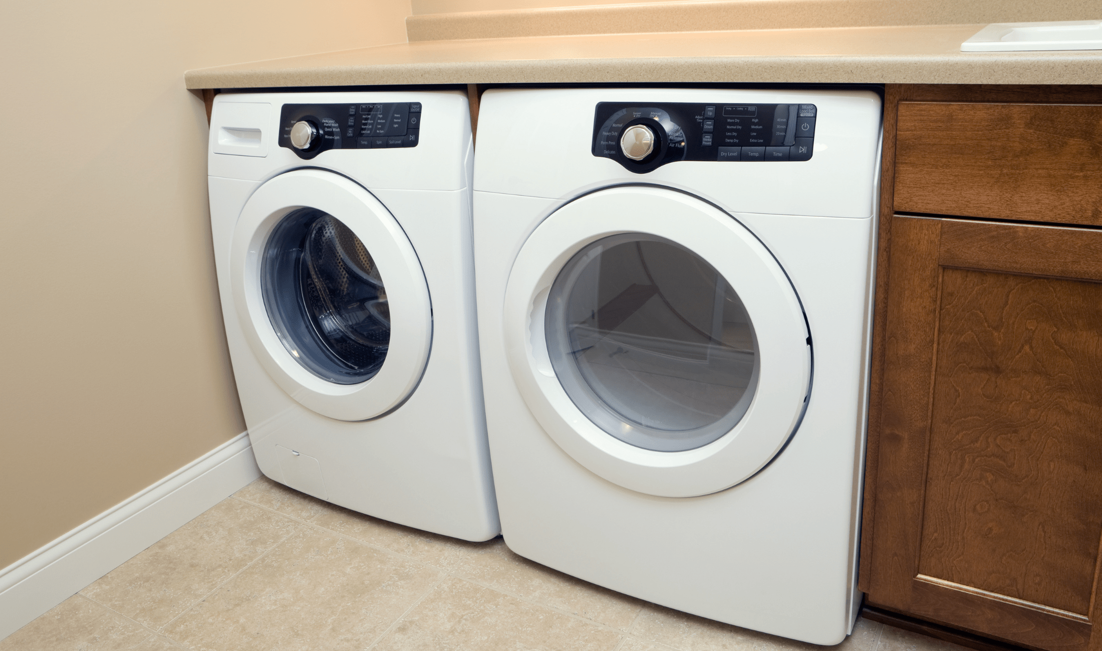 A washer and dryer next to each other beneath a counter.