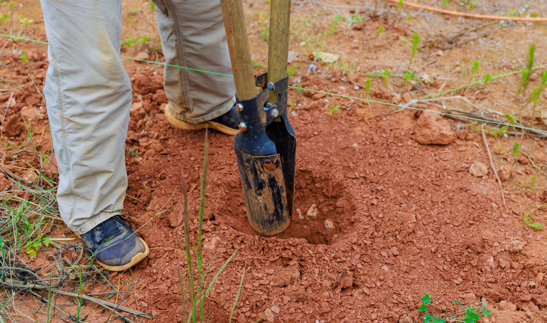 A person using a hole-digging tool to dig a fence post.