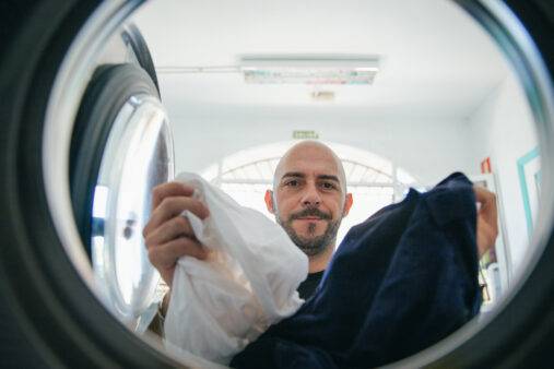 Man putting white and black clothes in washer.
