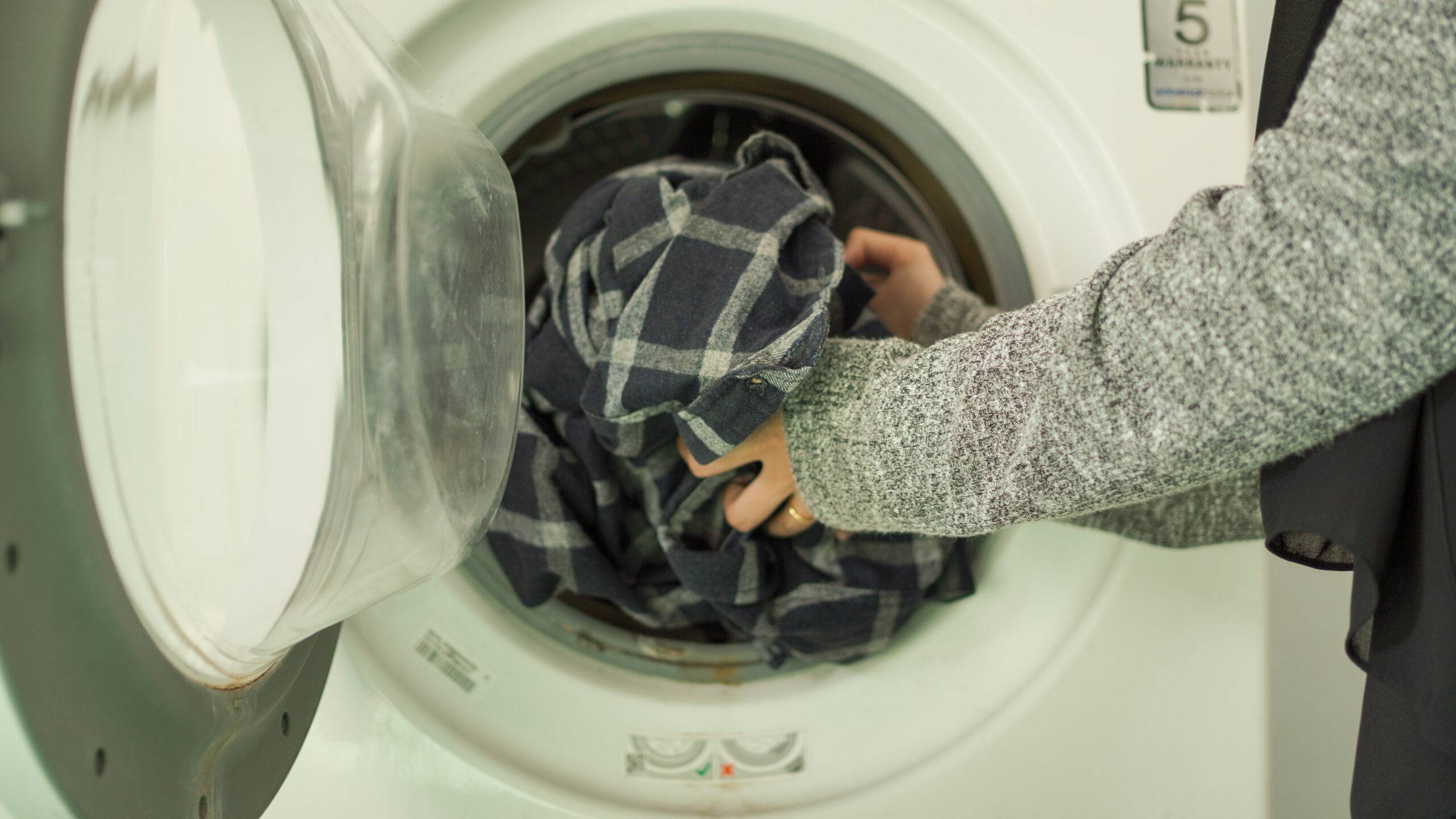 Person loading laundry into front-loader laundry machine.