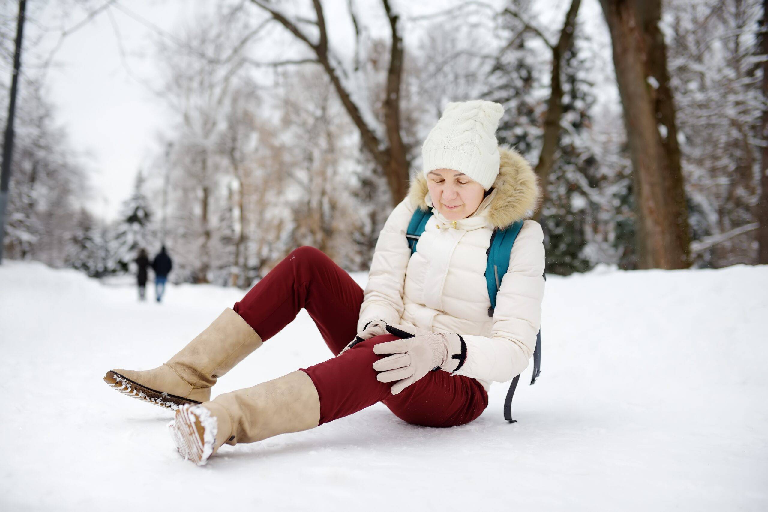 A woman sitting in the snow after falling and holding her leg.