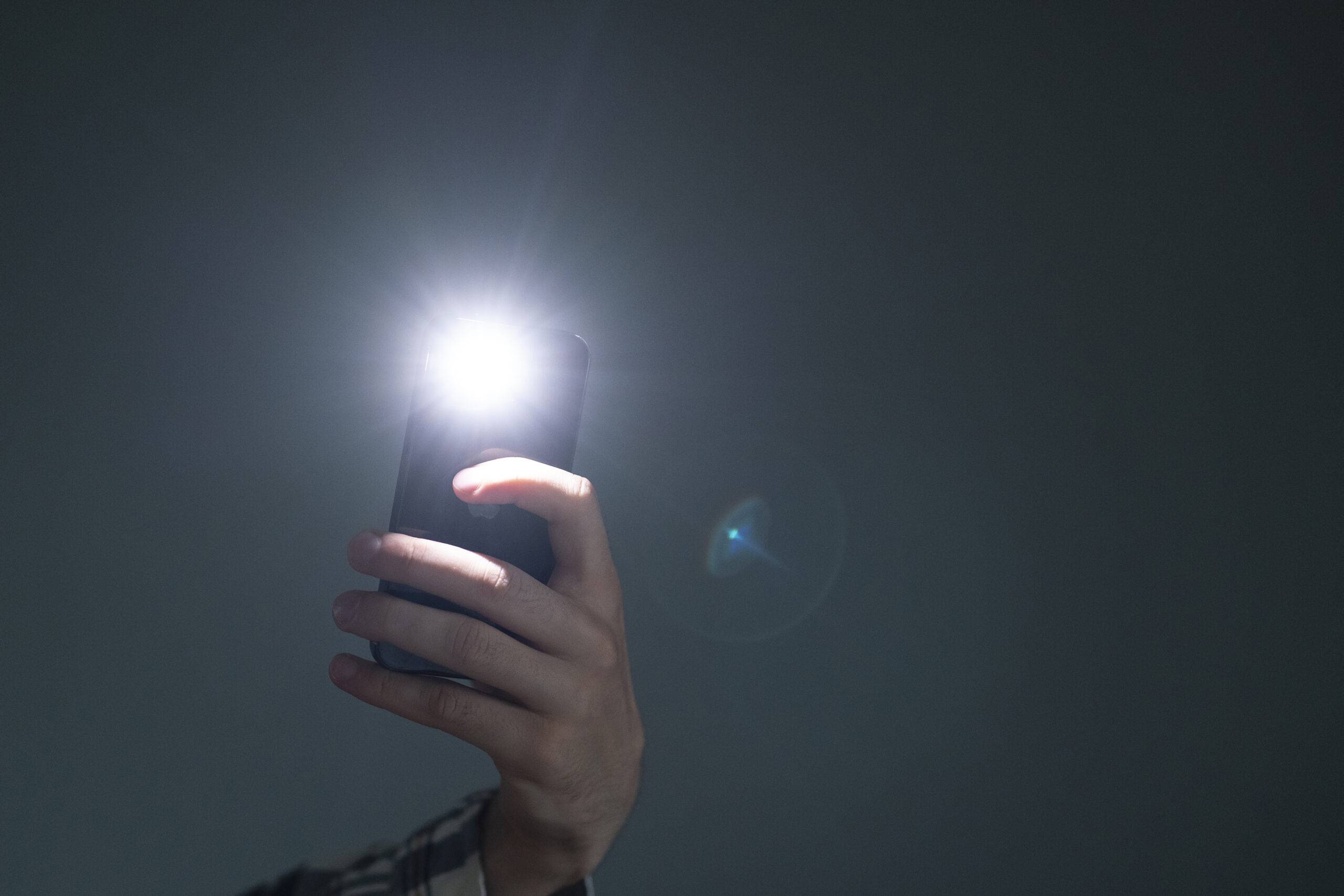hand holding a smartphone used as a torched, flashlight of mobile phone in the dark