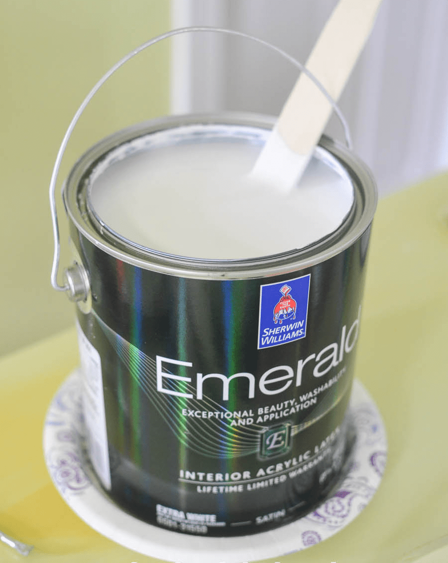 An open paint can with a stir stick in it. Beneath it is a paper plate.