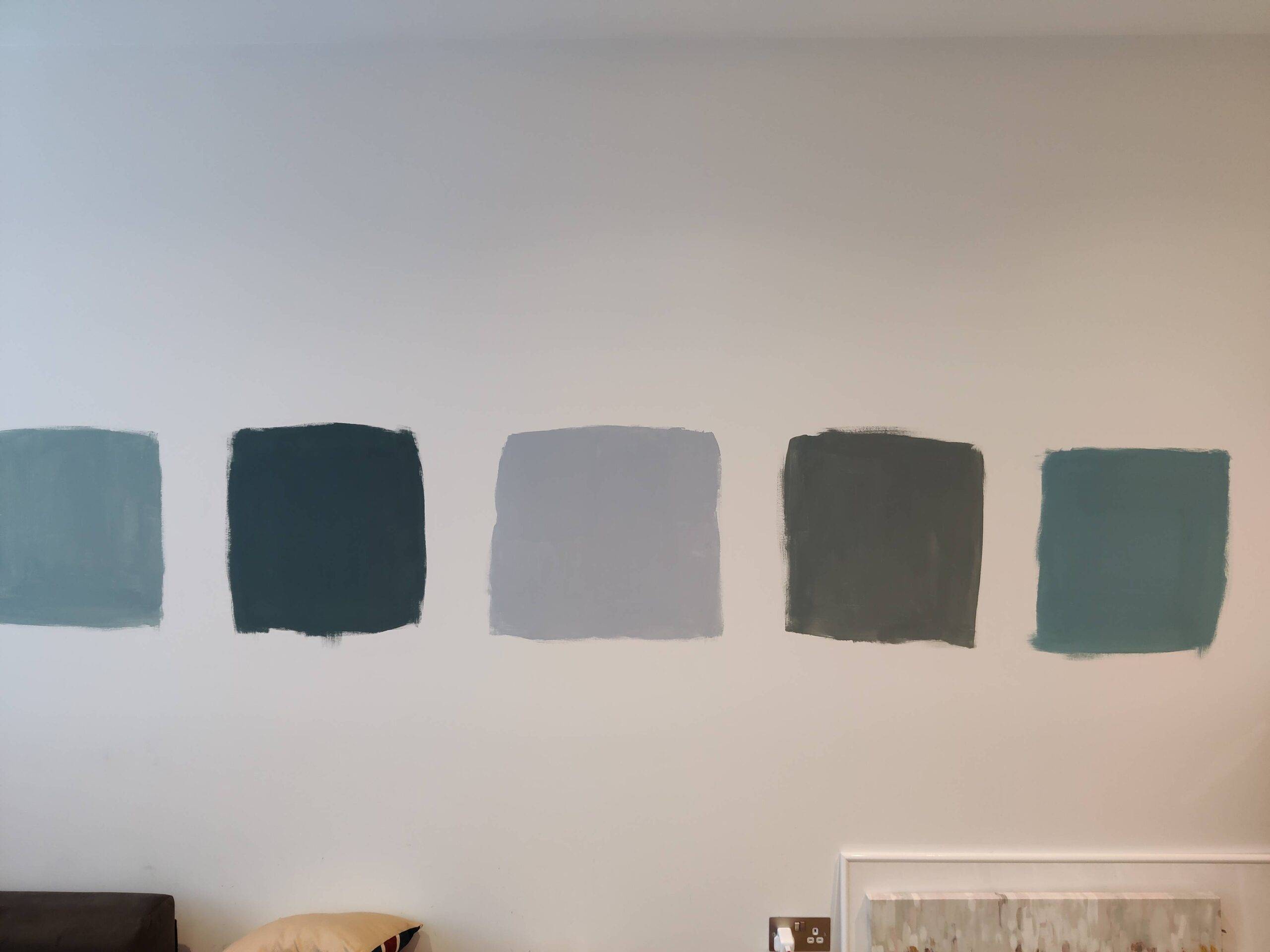 Five squares of different colors of blue paint in the middle of a white wall.