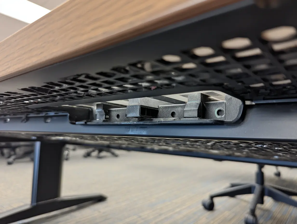 The underside of a table where a plastic cable management tray runs along.