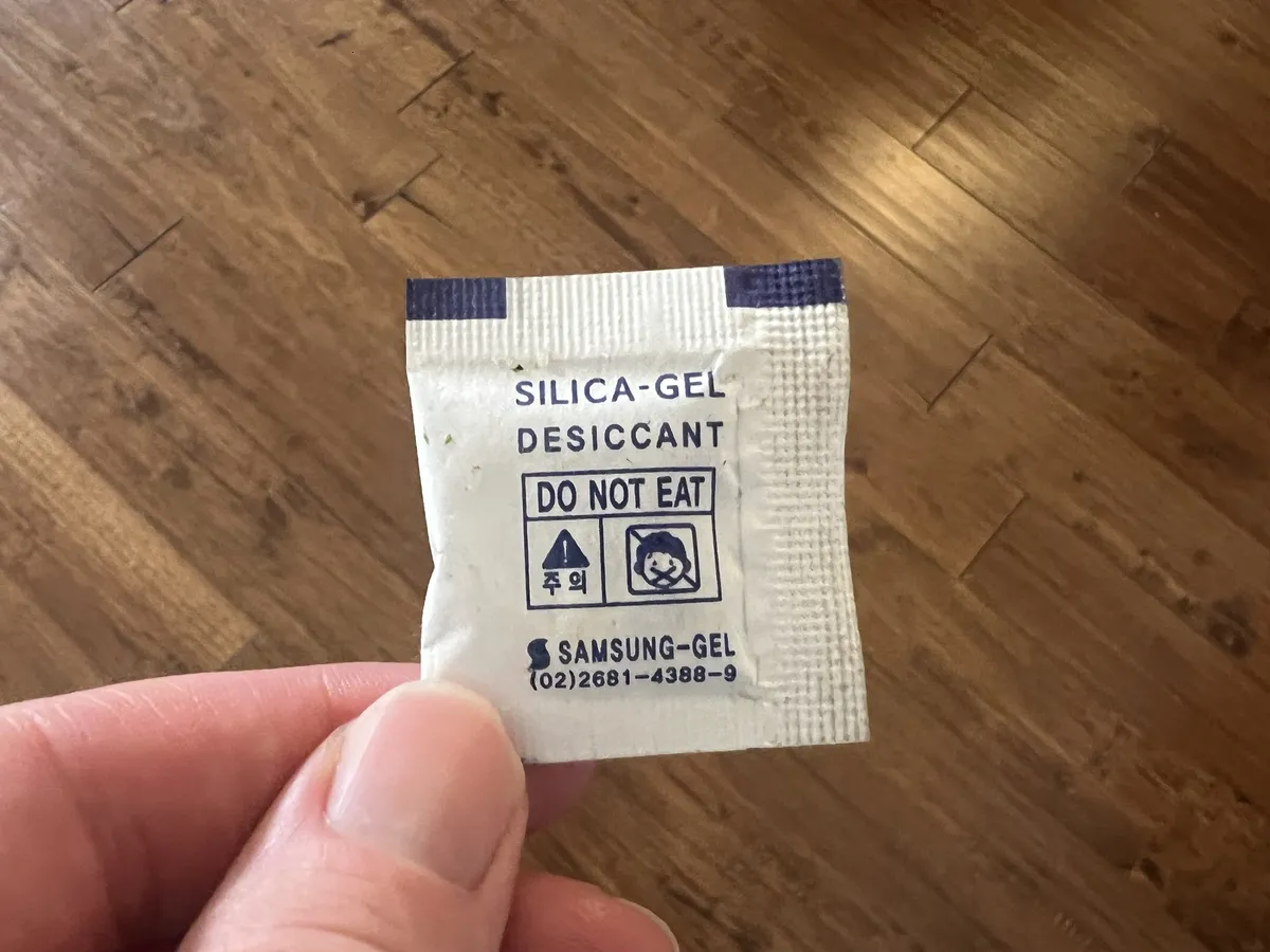 Close-up of a silica gel desiccant packet with warning label held in hand over a hardwood floor, Hillsdale, Reliez Valley, California, May 27, 2024. 