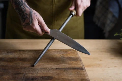 A man sharpening his knife using a honing rod.