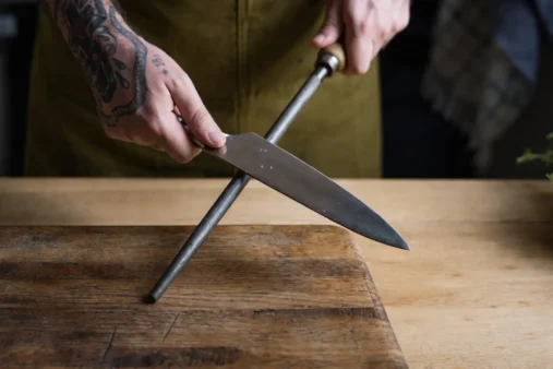 A man sharpening his knife using a honing rod.