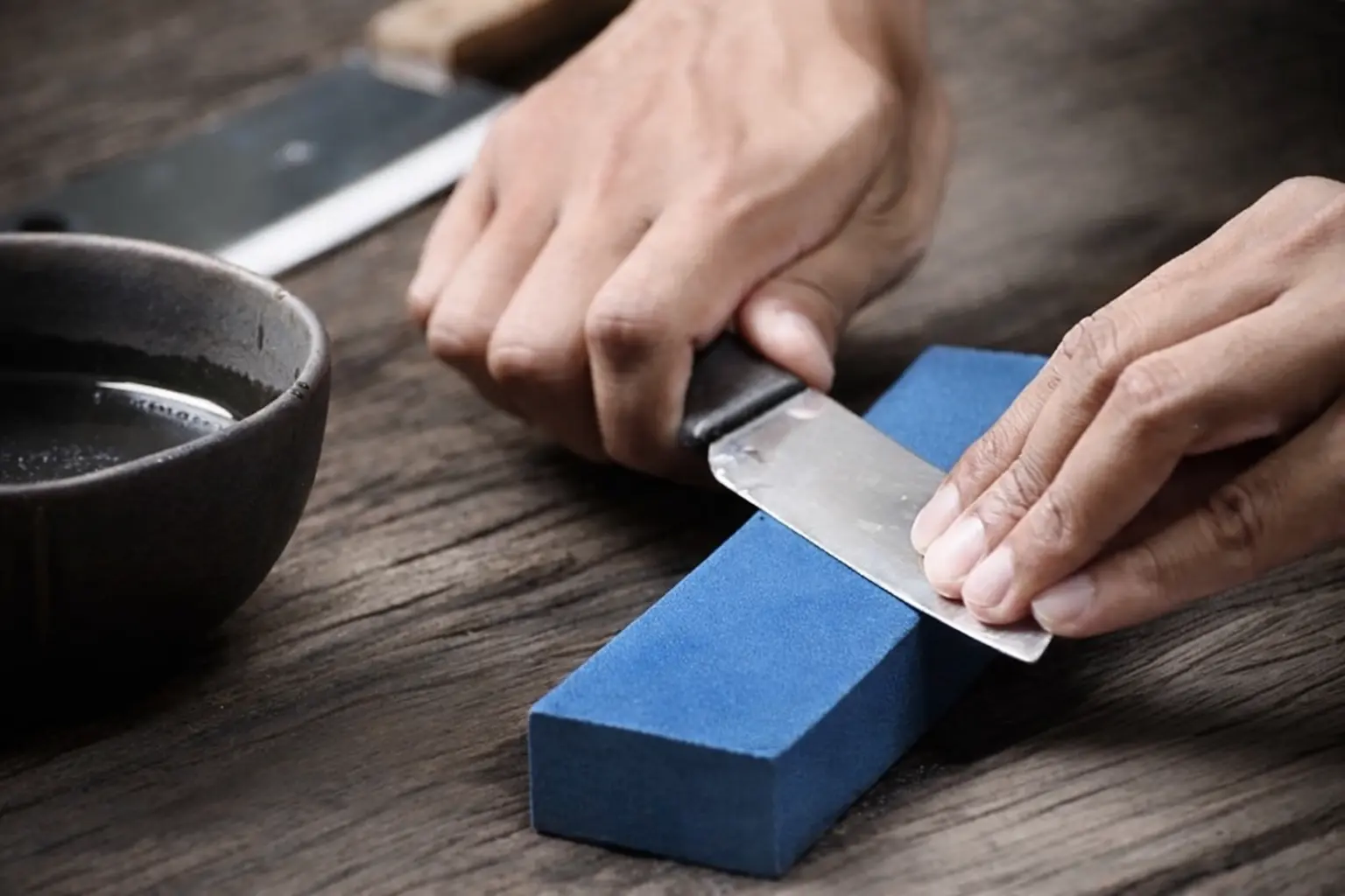 A person sharpening their knife using a whetstone.