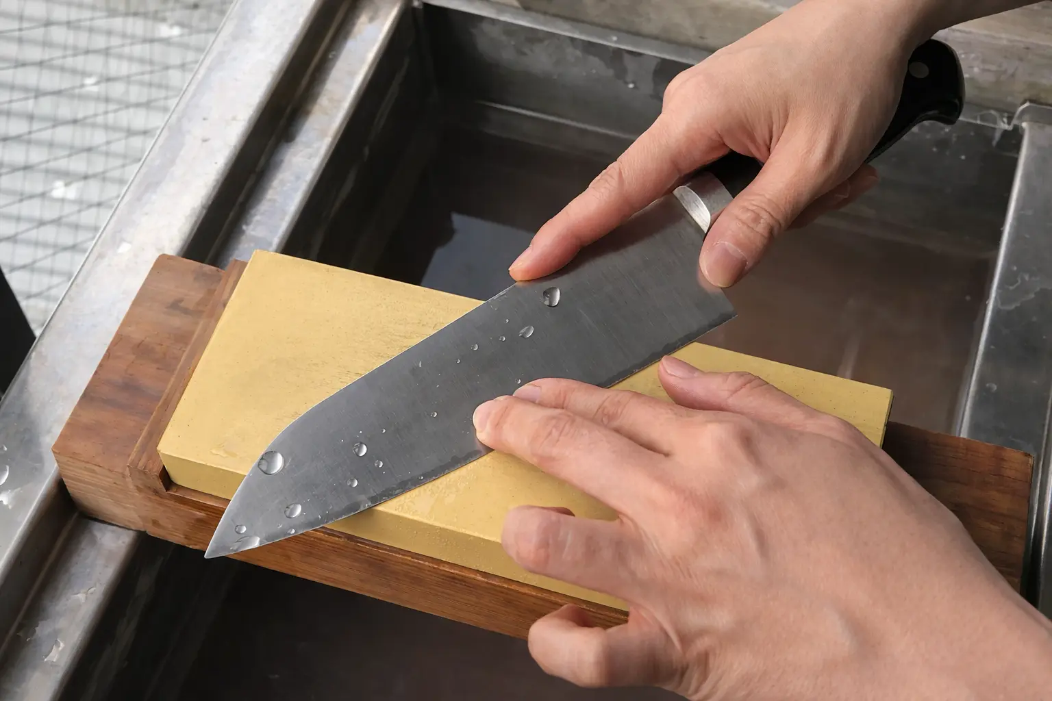 A person sharpening their knife using a whetstone.