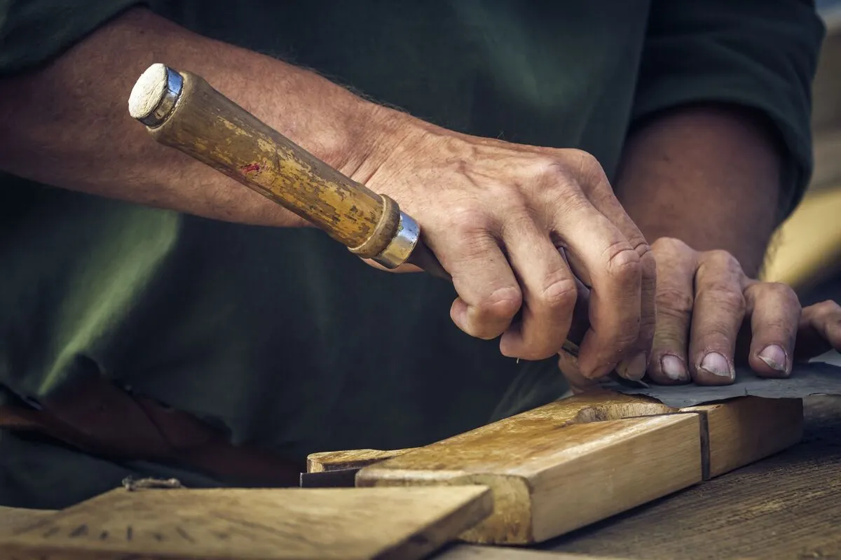 A man's hands using tools to carve from wood.