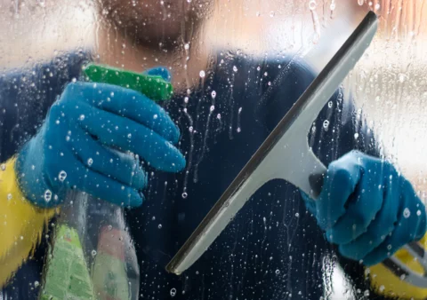 A man cleaning a glass surface using wipe and cleaning spray.