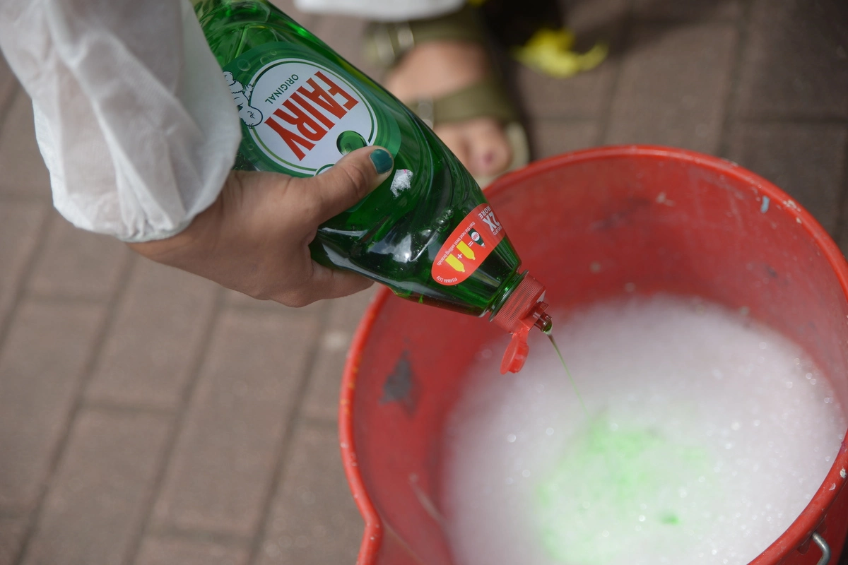 A woman's hand adding more cleaning liquid to an already frothy bucket of cleaning liquid. 