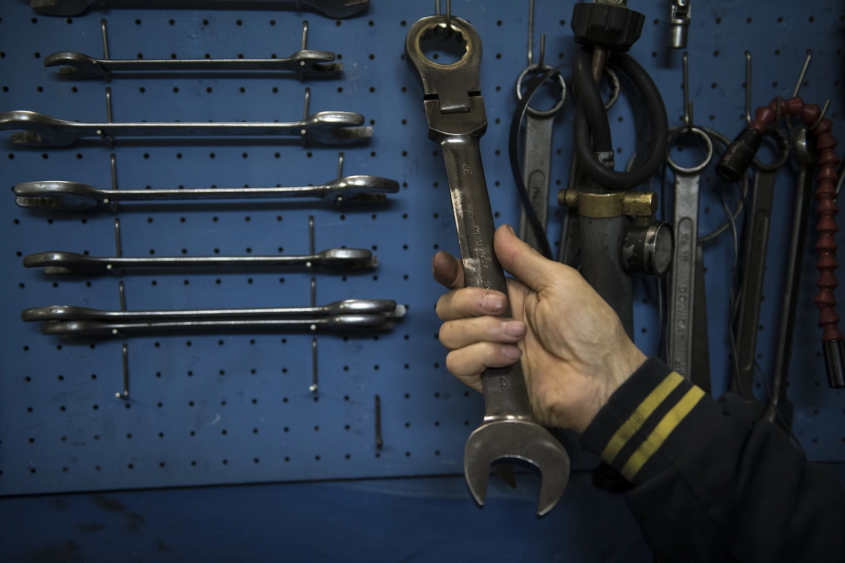 A man selecting a spanner from many tools on a peg board