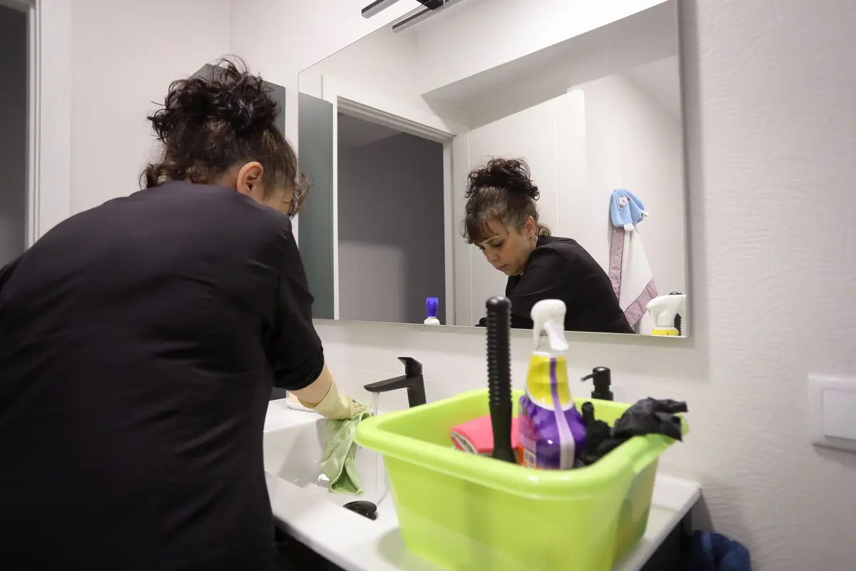 A woman wiping down the bathroom sink. She has necessary cleaning tools near her in a green basket.