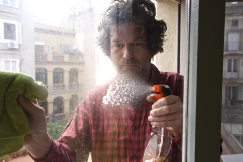 A man cleaning his window with spray solution and cloth.