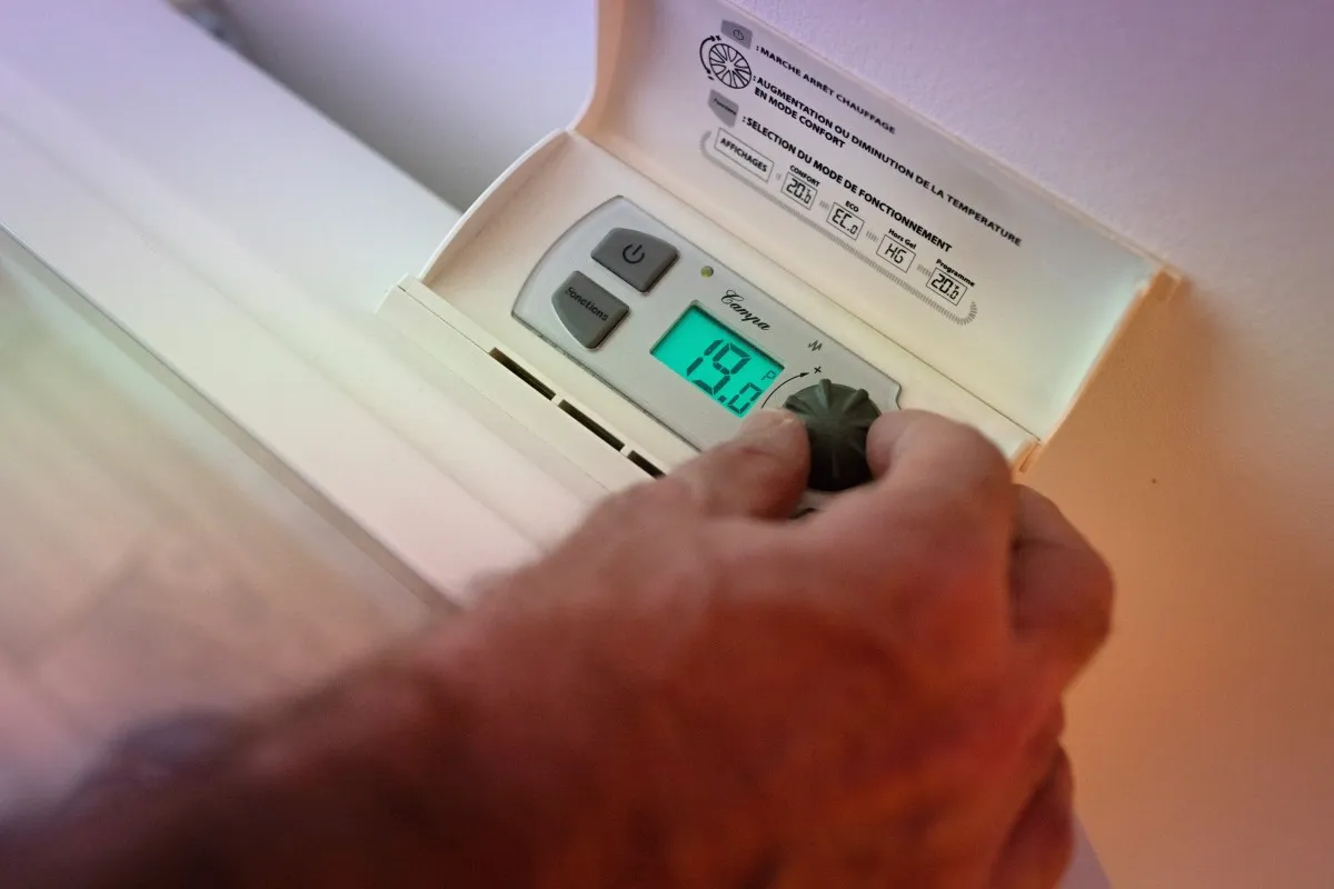 Someone setting the thermostat on an electric heater to 19 degrees. (